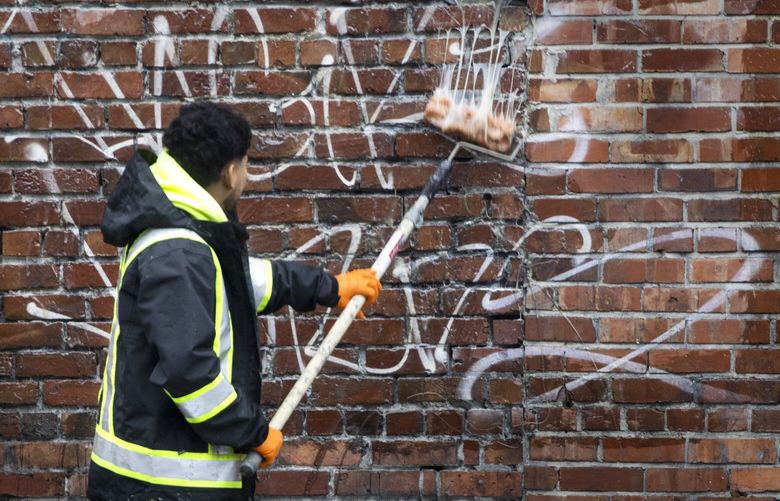 A man with Graffiti Busters removes graffiti on the brick wall of a building near the intersection of S. Jackson St. and 5th Ave. S. in Seattleâ€™s International District Monday, January 8, 2024. 225912