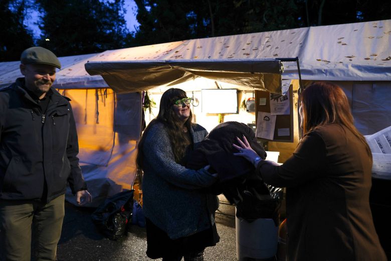 Cydney Moore, center, and Daniel Martin, left, both volunteers from the Burien Community Support Coalition, receive donated blankets and clothing from Burien resident Linda Clark at Sunnydale Village, a sanctioned encampment behind Oasis Home Church in Burien, on Dec. 14. (Karen Ducey / The Seattle Times)