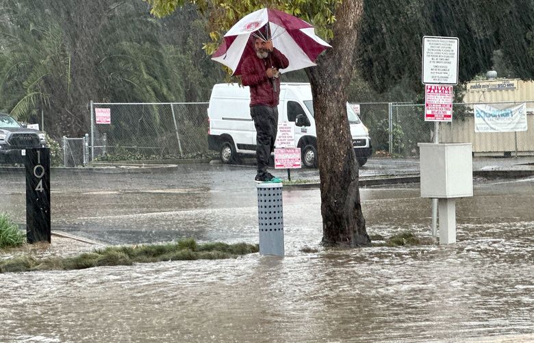 A man carrying an umbrella stands perched above a flooded street in Ventura, Calif., Sunday, Feb. 4, 2024. (AP Photo/Eugene Garcia) CAJC117 CAJC117