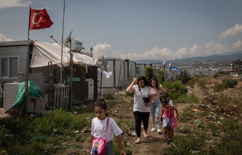 Adults walk children past a prefab container camp for the displaced to a new temporary school in Defne, a district near Antakya, Turkey, Sept. 11, 2023. On the anniversary of a catastrophic earthquake, Turkey is still struggling to rebuild, help survivors and hold people responsible for shoddy construction. (Nicole Tung/The New York Times) XNYT0544 XNYT0544