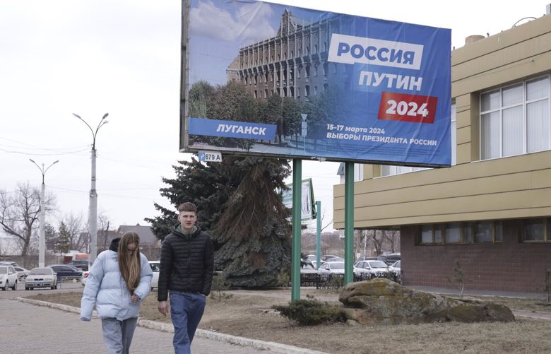 A couple walk past a billboard which promotes the upcoming presidential election with words in “Russian: Russia, Putin, 2024” in a street in Luhansk, the capital of Russian-controlled Luhansk region, eastern Ukraine, on Thursday, March 14, 2024. Russian President Vladimir Putin Thursday called on people in Ukraine’s occupied regions to vote, telling them and Russians that participation in the elections is “manifestation of patriotic feeling,” Presidential elections are scheduled in Russia for March 17. (AP Photo) XEST112 XEST112