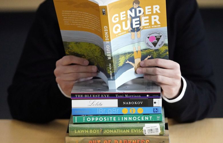 FILE – Amanda Darrow, director of youth, family and education programs at the Utah Pride Center, poses with books that have been the subject of complaints from parents on Dec. 16, 2021, in Salt Lake City. Kabobe’s graphic memoir “Gender Queer” continues its troubled run as the country’s most controversial book, topping the American Library Association’s “challenged books” list for a third straight year.  (AP Photo/Rick Bowmer, File) NYET450 NYET450