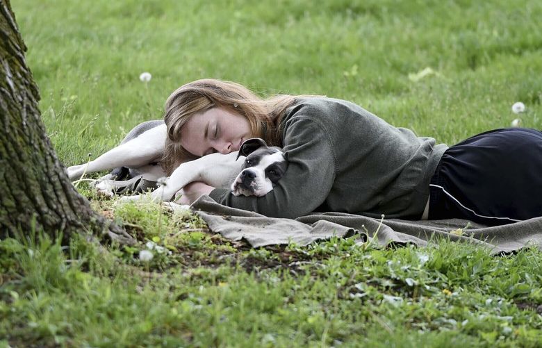 FILE -A woman and her dog nap between rain showers at Schenley Park, Tuesday, May 4, 2021 in Pittsburgh. The Gallup survey, released Monday, April 15, 2024, says that a majority of Americans say they would feel better if they could have more sleep. But in the U.S., where the ethos of grinding and pulling yourself up by your own bootstraps is ubiquitous, getting enough sleep can seem like a dream.(Pam Panchak/Pittsburgh Post-Gazette via AP, File) PAPIT301 PAPIT301