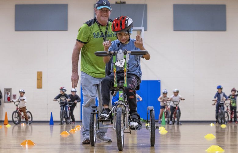 Ethan Gray, a paraeducator, helps nine-year-old Adiel Ortega, a Gregory Heights elementary student, to learn safety tips and how to ride a bike in his P. E. Class Friday, April 19, 2024.  The Cascade Bicycle Club was also there to help with the class;

The Washington statewide bike riding program prioritizes schools with the highest need, with a goal of improving public health, and teaching youth the essential skills of walking, biking, and mass transit as primary forms of mobility.
 226666