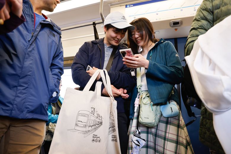 Holding bags they picked up at the Redmond Technology Station, Paul Wang, left, and Alison Wu ride the Eastside light rail 2 Line on opening day Saturday. They both work at Microsoft.  (Karen Ducey / The Seattle Times)