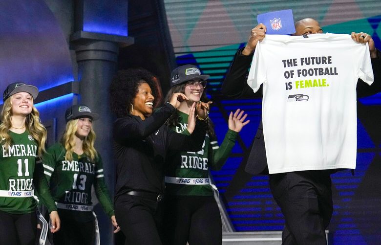Seattle Seahawks wide receiver Tyler Lockett, right, walks on stage with Seattle’s Emerald Ridge girls flag football team during the third round of the NFL football draft, Friday, April 26, 2024, in Detroit. (AP Photo/Jeff Roberson) NVJL163