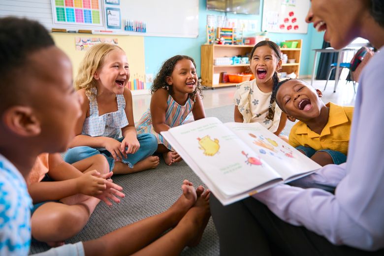 A teachers reads a book aloud to her happy students sitting on the floor with her.