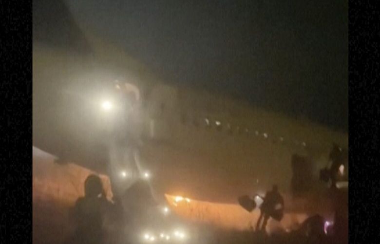 In this grab taken from video people jump down emergency slides, running from a plane, in Dakar, Senegal, Wednesday, May 8, 2024. A Boeing 737 plane carrying 85 people caught fire and skidded off a runway at the airport in Dakar, Senegal’s capital, injuring 10 people. (Cheick Siriman Sissoko via AP) 