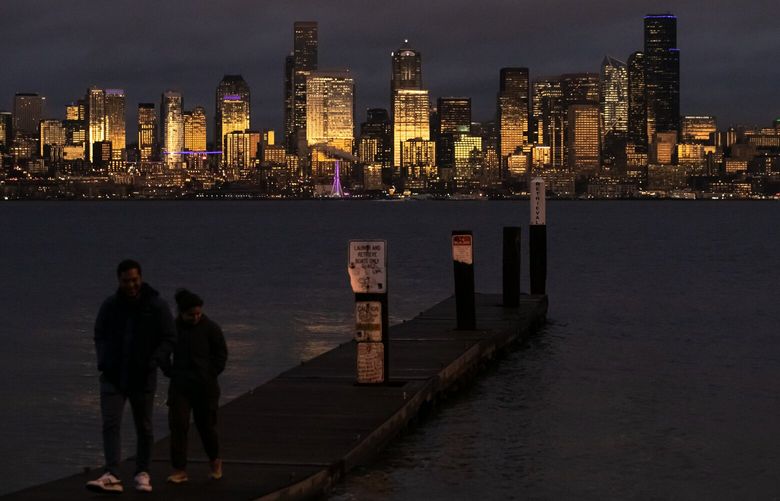 Nasser Abdala, right, and Anggi Giraldo walk on the Don Armeni Boat Ramp during sunset in West Seattle Tuesday, Nov. 22, 2022. Drivers and pedestrians stopped to take photos of the shaft of light that illuminated the Seattle skyline against moody skies. 
LO 222268