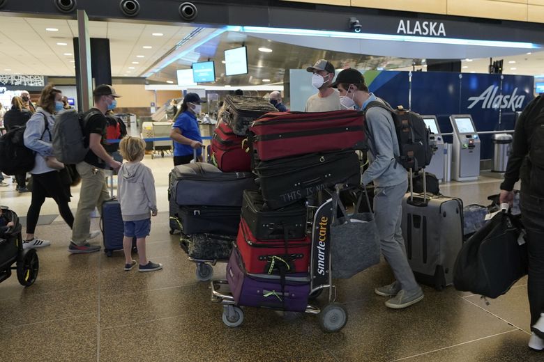 Passengers wearing masks walk with luggage near an Alaska Airlines check-in area at Seattle-Tacoma International Airport in Seattle. (Ted S. Warren / The Associated Press, 2021)