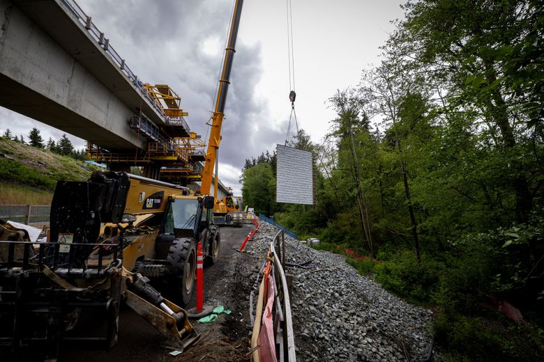 A wall is lifted into place on June 3 at the longest bridge in the Link light rail system, 1,100 feet long, during construction along wetlands near Federal Way, at right, that have made the engineering of the project a challenge. (Ken Lambert / The Seattle Times)
