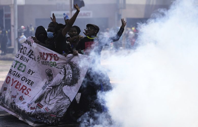 Protesters hide behind a banner as police fire tear gas at them during a protest over proposed tax hikes in a finance bill in downtown Nairobi, Kenya Tuesday, June 25, 2024. (AP Photo/Brian Inganga) KBI118 KBI118