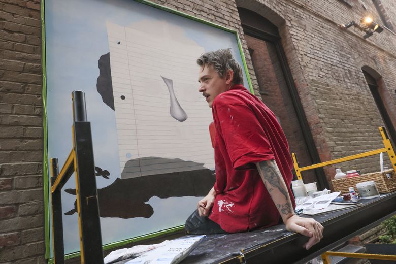 Artist Brandon Vosika takes a break from creating a mural in the alley of RailSpur, a three-building development in Pioneer Square. (Ivy Ceballo / The Seattle Times)