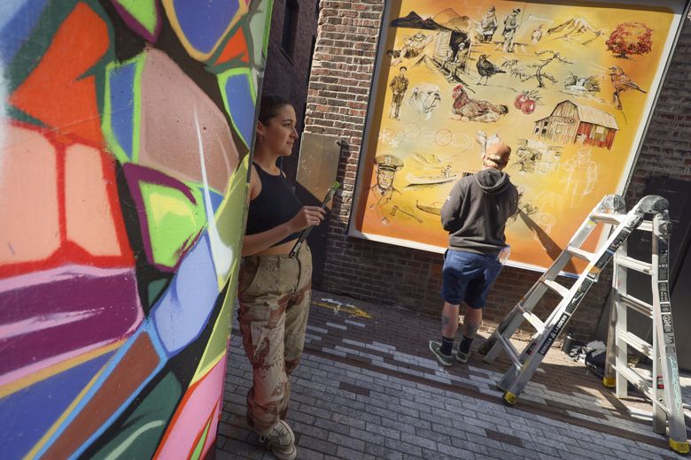 Artists Sanoe Stevenson-Egeland, left, watches a band perform during a break in painting while Zach Rockstad, right, paints a mural, part of a public art installation presented by Forest For The Trees. (Ivy Ceballo / The Seattle Times)