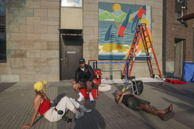 Artists Becca Fuhrman, John Sarkis and Kyler Martz take a break together near Martz’s mural, part of a public art installation presented by Forest For The Trees and ARTXIV. (Ivy Ceballo / The Seattle Times)