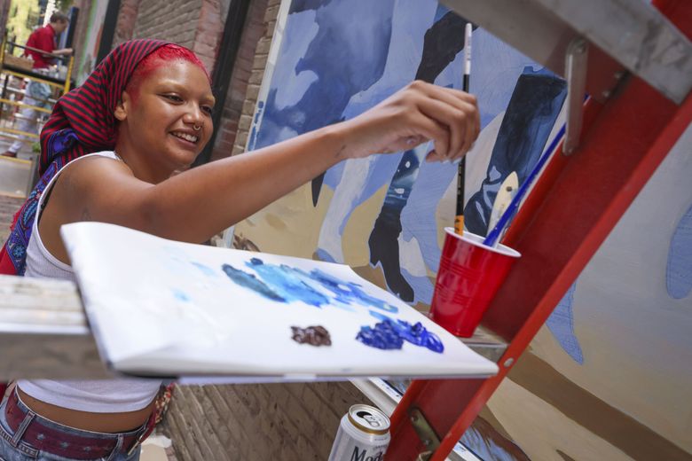 Artist Chloe King paints a mural presented by Forest For The Trees. (Ivy Ceballo / The Seattle Times)