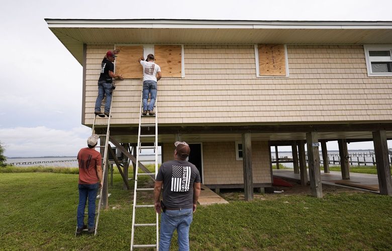 Jerry McCullen, top of ladder left, and Carson Baze, top of ladder right, put plywood over the windows of a house ahead of Hurricane Helene, expected to make landfall Thursday evening, in Alligator Point, Fla., Wednesday, Sept. 25, 2024. (AP Photo/Gerald Herbert) FLGH116 FLGH116