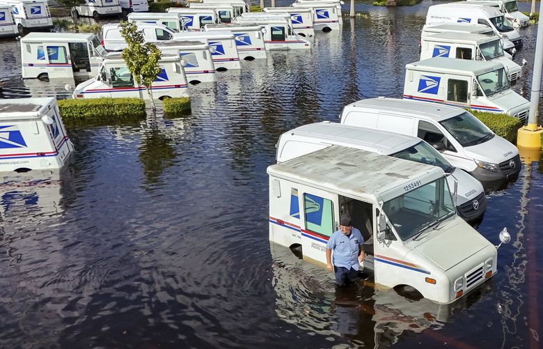 A USPS worker inspects trucks that had been relocated to protect them from wind but which are now underwater as intense rain from Hurricane Milton caused the Anclote River to flood, Friday, Oct. 11, 2024, in New Port Richey, Fla. (AP Photo/Mike Carlson) FLMC109 FLMC109