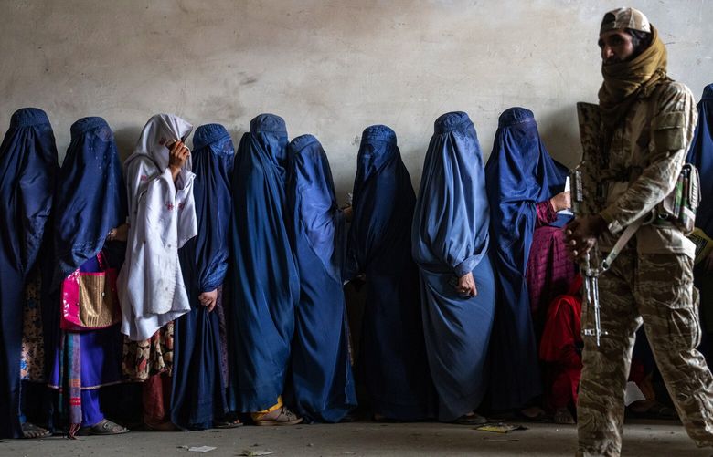 FILE – A Taliban fighter stands guard as women wait to receive food rations distributed by a humanitarian aid group, in Kabul, Afghanistan, on May 23, 2023. Human Rights Watch said Monday, Feb. 12, 2024 that Afghanistan’s public health system has been hit hard following a sharp reduction in foreign assistance, coupled with serious Taliban abuses against women and girls, jeopardizing the right to healthcare of millions of Afghans. (AP Photo/Ebrahim Noroozi, File)