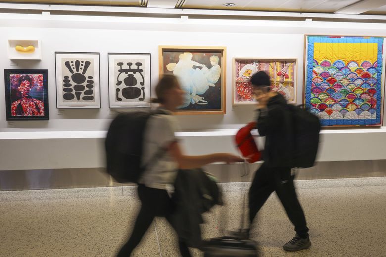 Travelers walk past a gallery display next to the Seattle–Tacoma International Airport’s first all-gender bathroom. (Ivy Ceballo / The Seattle Times)