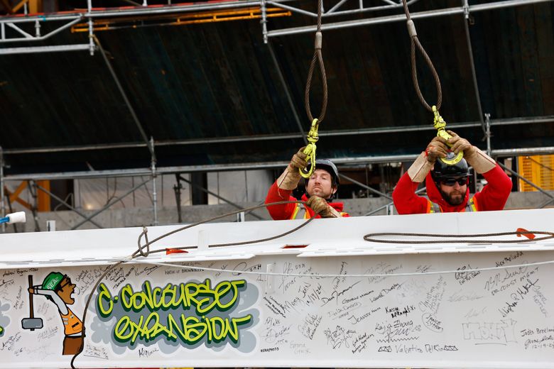 Ironworkers rig one of the final steel beams that bears the signatures of people who worked on the C Concourse Expansion Project during a &#8220;topping out&#8221; ceremony at Sea-Tac Airport on Thursday. Turner Construction Company and Apex Steel used a crane to put the beam in place atop the highest point. (Karen Ducey / The Seattle Times)