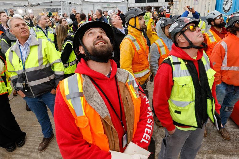 Ironworkers Dustin Irwin, left, and Steve Dupee watch as Turner Construction Co., and Apex Steel use a crane to put one of the final steel beams in place atop the highest point of C Concourse Expansion Project. (Karen Ducey / The Seattle Times)