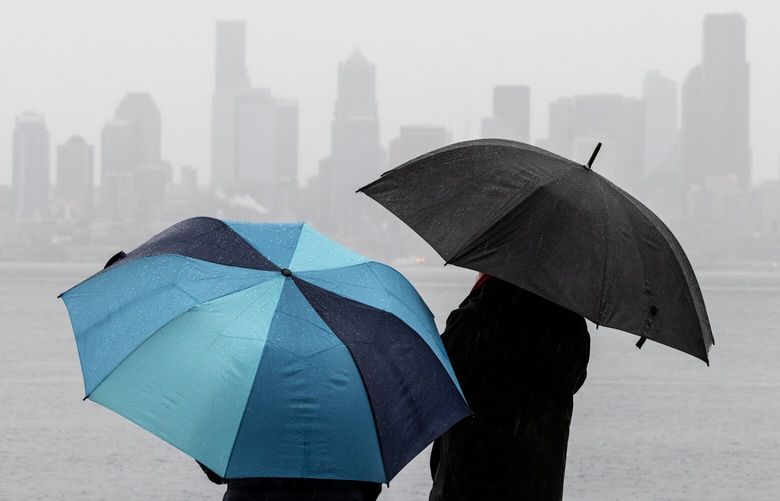 With downtown Seattle in the background, Michael Rose, right, chats with a friend visiting from Canada, Tania Minaeva, as the two watch Rose’s wife Irina take her almost daily swim in Elliott Bay as rains intensify, Wednesday afternoon, Dec. 25, 2024 in West Seattle. A major atmospheric river is forecast.
