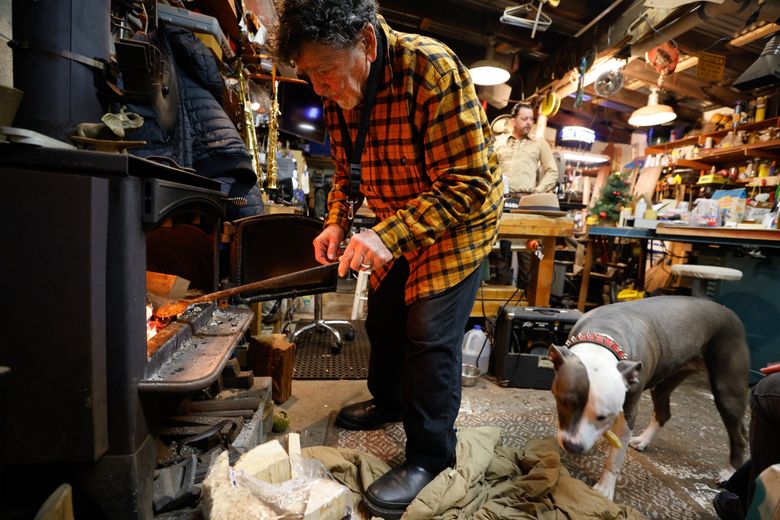 Rick Fabano adds wood to the stove, and Pea-oui chews on a stick while friends ring in the new year in woodshop they call the Rocket Shop at Sagstad Marina in Seattle. Rick lived 30 years on a boat in Ballard. (Karen Ducey / The Seattle Times)