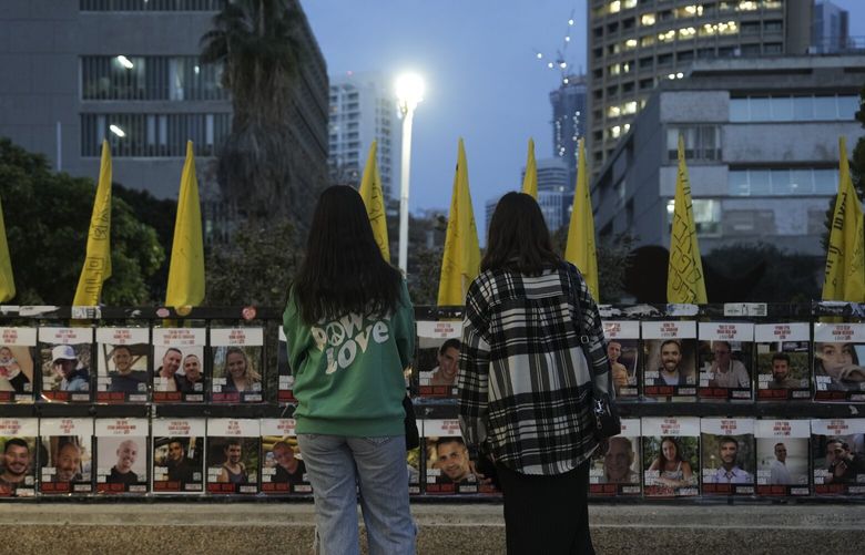 Two women observe photos of hostages held in the Gaza Strip, which are plastered to a fence in Tel Aviv, Israel, Wednesday, Jan. 15, 2025. (AP Photo/Oded Balilty) BA101 BA101