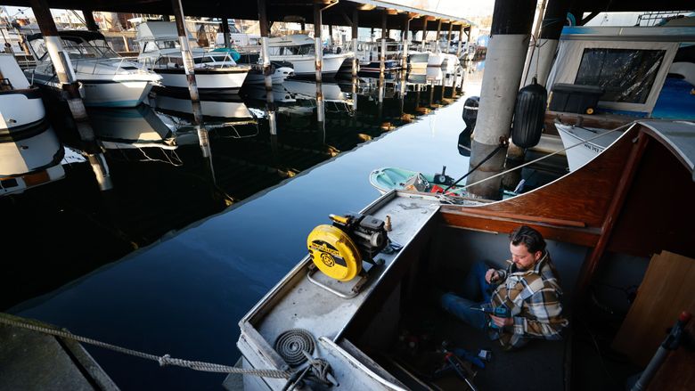 Ryan Currier works on his boat, Elwood, securing the feed line to his diesel heater in Sagstad Marina. He has lived on his boat since 2019 as a way to afford life in Ballard. (Karen Ducey / The Seattle Times)