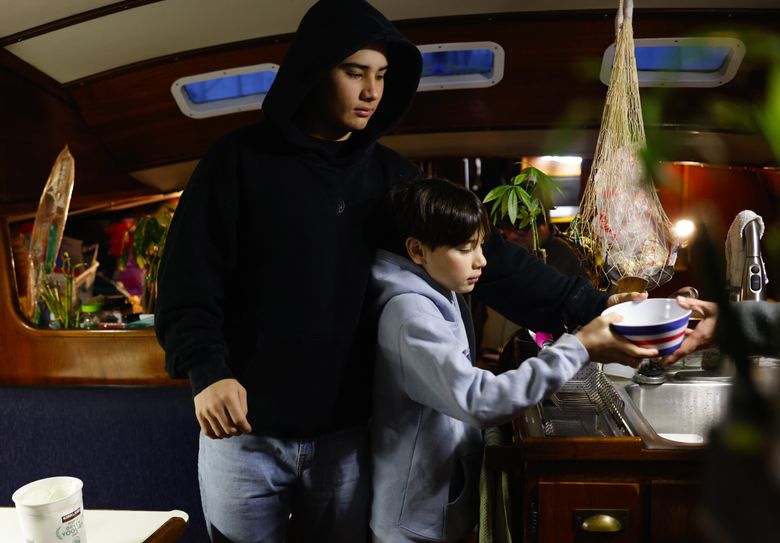 Aiden DePaula. 18, reaches over his brother Ze, 12, to grab a bowl for breakfast from their mom, Rie, on the sailboat the family lives on  — along with their dog and two cats  — at Shilshole Bay Marina. (Karen Ducey / The Seattle Times)