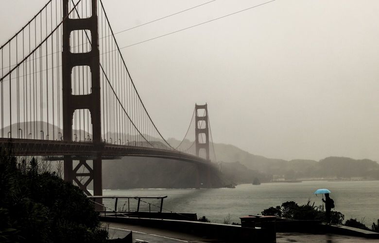 A man walks with umbrella near the Golden Gate Bridge during a rainstorm in San Francisco on Tuesday, Feb. 4, 2025. (Gabrielle Lurie/San Francisco Chronicle via AP) CAFRA106 CAFRA106