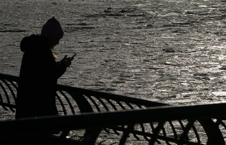With the Statue of Liberty in the background, a woman uses her phone to record ice on the Hudson River in New York, Wednesday, Jan. 22, 2025. (AP Photo/Seth Wenig) NYSW101 NYSW101