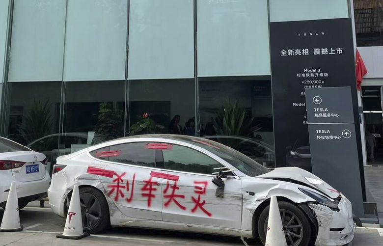 This photo provided by Zhang Yazhou shows her damaged Tesla Model 3, right, parked outside of the Tesla dealership in Zhengzhou, the capital of central China’s Henan province, on March 10, 2021. The car was painted with the phrase, “Brakes fail.” (Zhang Yazhou via AP) NY373 NY373