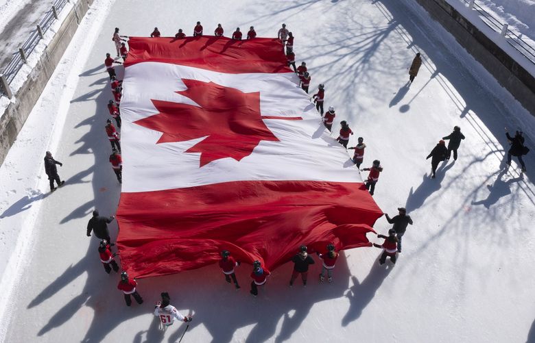 Local youth skate with a large Canadian flag on the Rideau Canal to launch celebrations for the 60th Anniversary of the National Flag of Canada Day, Friday, Feb. 14, 2025 in Ottawa. (Adrian Wyld /The Canadian Press via AP) AJW107 AJW107 (Adrian Wyld / The Associated Press)