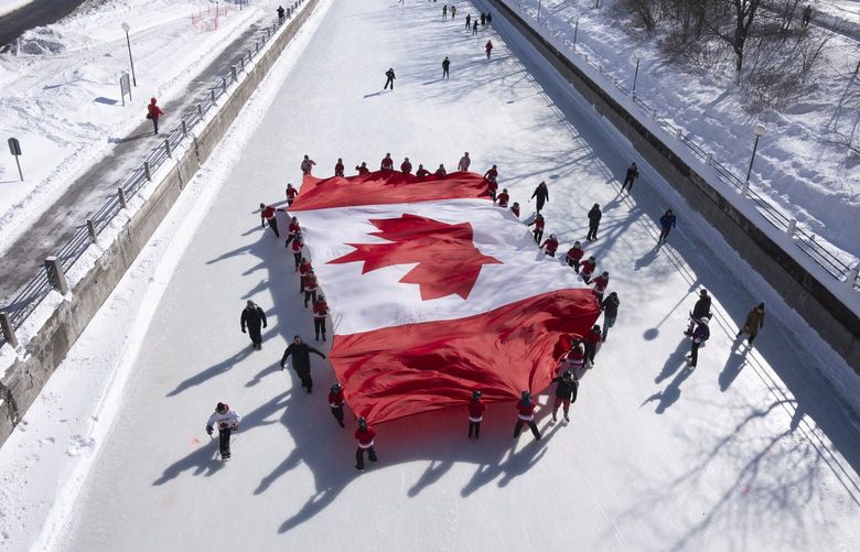 Local youth skate with a large Canadian flag on the Rideau Canal to launch celebrations for the 60th Anniversary of the National Flag of Canada Day, Friday, Feb. 14, 2025 in Ottawa.  (Adrian Wyld/The Canadian Press via AP) AJW104 AJW104
