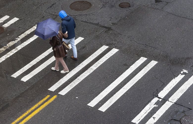 Under cloudy and rainy skies, a couple crosses Yesler Way between 1st Avenue South and 2nd Ave South on Feb. 17, 2025, in Seattle. (Ellen M. Banner / The Seattle Times)