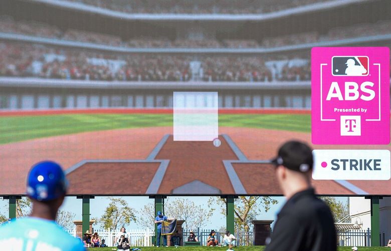 Kansas City Royals first base coach Damon Hollins and umpire Chris Guccione look on as the results of a Automated Ball Strike (ABS) replay challenge by Texas Rangers catcher Chad Wallach are shown on the scoreboard during the eighth inning of a spring training game at Surprise Stadium on Friday, Feb. 21, 2025, in Surprise, Arizona.  Wallach successfully challenged a called ball. (Smiley N. Pool/The Dallas Morning News/TNS) 135707196W 135707196W