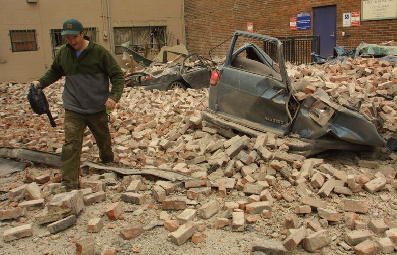 After yesterday’s eathquake, Jim Cudney of Lynnwood retrievs the purse belonging to a fellow worker from inside their van, which was crushed by bricks falling from building across from the Exhibition Center, where they were setting up for the RV show. Another car, background, was also crushed. (2/28/2001)