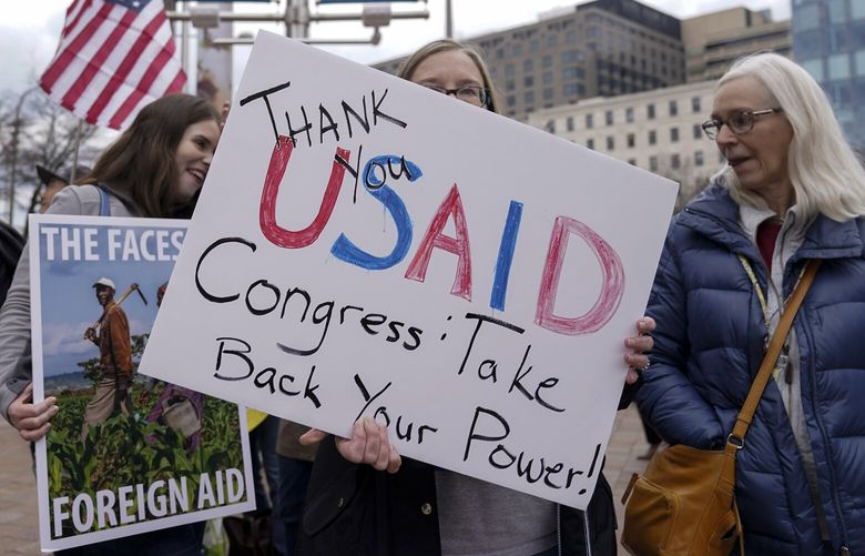 Supporters hold up their signs as United States Agency for International Development (USAID) workers, carry their personal belongings after retrieving them from the USAID’s headquarters in Washington, Thursday, Feb. 27, 2025. (AP Photo/Jose Luis Magana) DCJL136 DCJL136