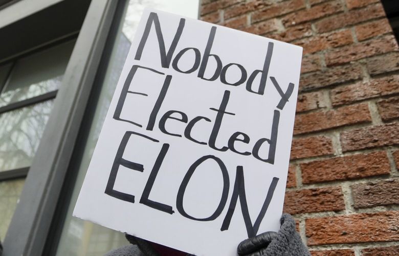 A person protesting Elon Musk’s actions in the Trump administration holds a sign outside a Tesla showroom in Seattle on Thursday, Feb. 13, 2025. (AP Photo/Manuel Valdes) XMV105 XMV105