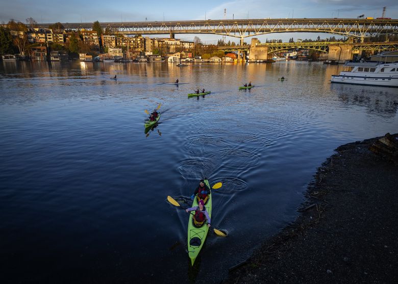 With sunrise hitting the Ship Canal and University bridges in the background, kayaks arrive before 7:30 a.m. at Fritz Hedges Waterway Park during the opening leg of the “unofficial” Seattle heptathlon on March 25 in Seattle. (Ken Lambert / The Seattle Times)