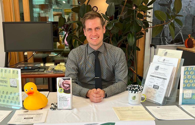 A smiling person in shirt and tie sits at a table with branding resources.