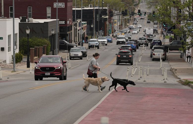A woman and her dogs cross 31st Street in Kansas City, Mo., where the city implemented a “road diet” reducing the street from four lanes to two in an effort to reduce speeding and accidents, Thursday, April 17, 2025. (AP Photo/Charlie Riedel) KSCR102 KSCR102