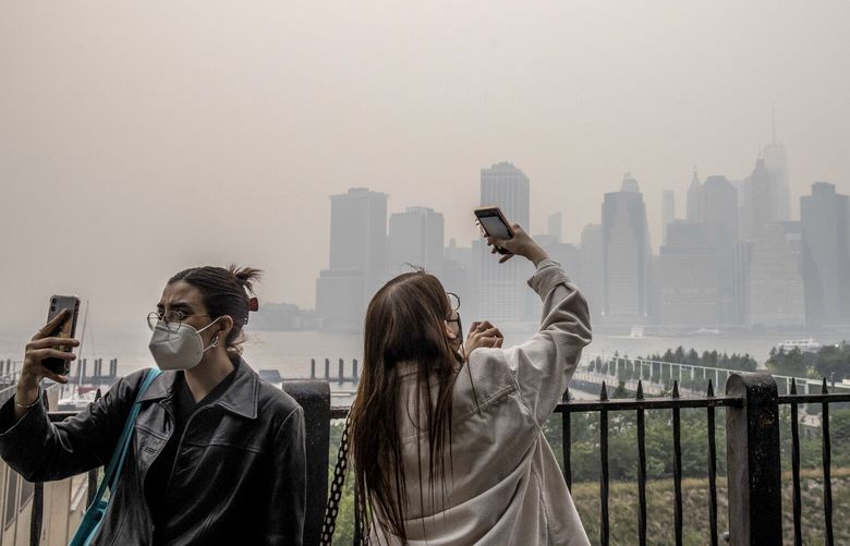 FILE — People take pictures on the Brooklyn Promenade as smoke from northern wildfires blankets Lower Manhattan, June 7, 2023. At least 156 million Americans, about 46 percent of the population, live with unsafe levels of ozone, particulate pollution or both, according to the American Lung Association’s annual State of the Air report. (Dave Sanders/The New York Times)