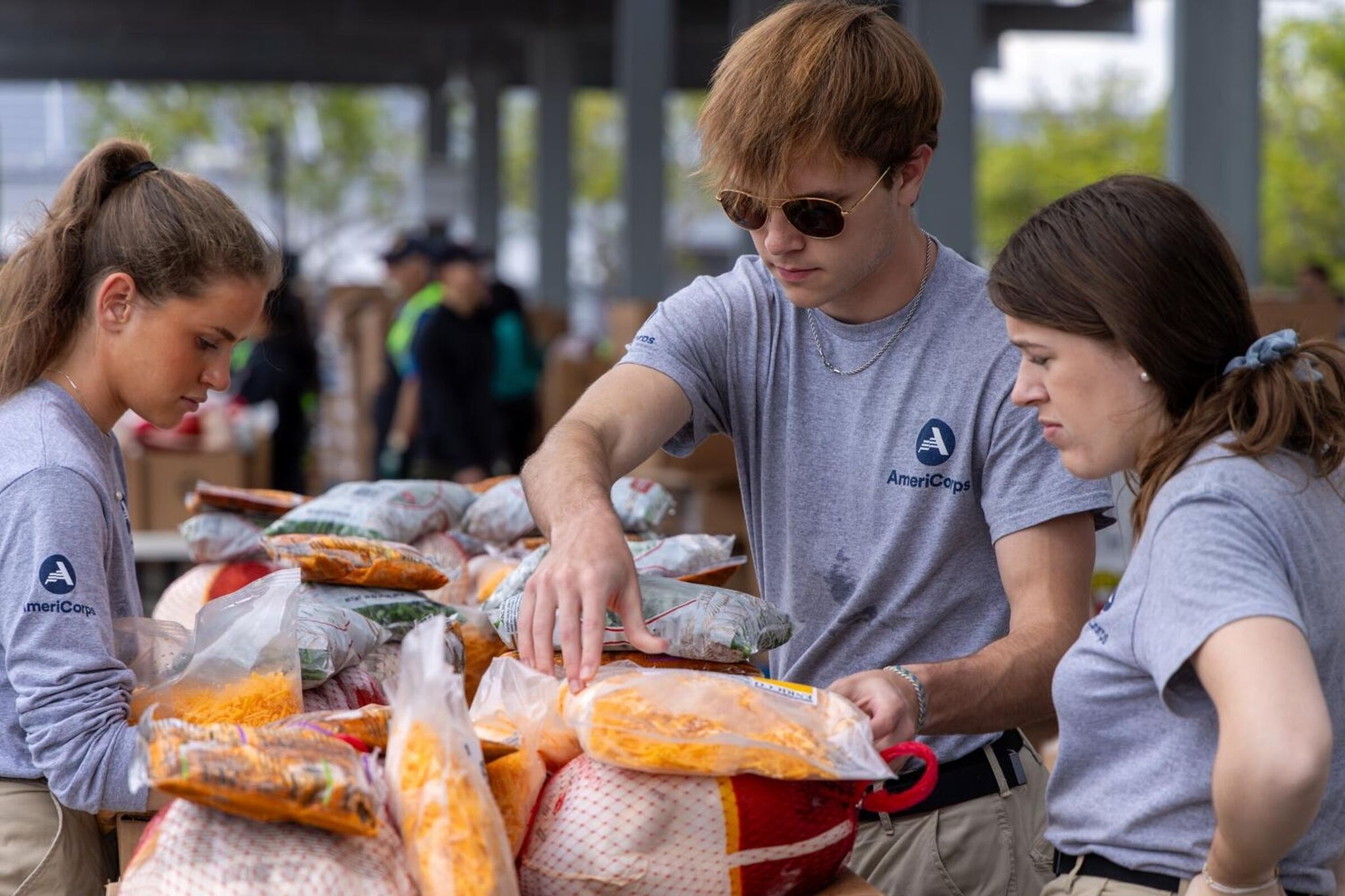 Участники AmeriCorps Бибианна МакКоноулог, слева, Бобби Харрисон и Сара Мерфи готовят продовольственный пакет с индейкой, сыром, специями, зелёной фасолью, яблоками и коробкой с фруктами для раздачи на мероприятии ко Дню благодарения в 2023 году в... (Ирфан Хан/Los Angeles Times/TNS)Подробнее