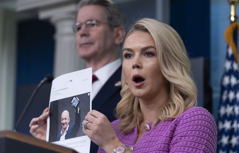 White House press secretary Karoline Leavitt with Treasury Secretary Scott Bessent, back left, shows a picture of Jeff Besos as she responds to a question about Amazon, during a briefing in the James Brady Press Briefing Room at the White House, Tuesday, April 29, 2025, in Washington. (AP Photo/Manuel Balce Ceneta) DCMC101 DCMC101