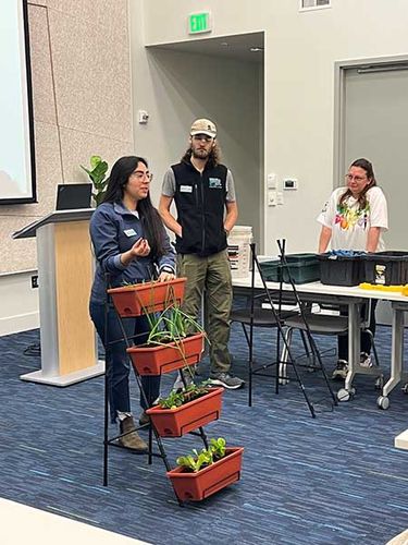 A woman shows a vertical planting system in a classroom.