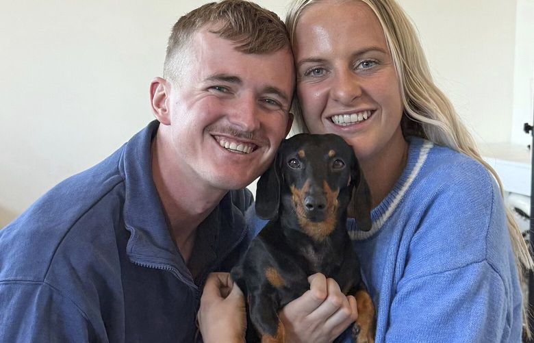 Georgia Gardner and partner Josh Fishlock hold Valerie, their miniature dachshund after being reunited on Kangaroo Island in South Australia after Valerie was missing for 540 days, Tuesday, May 6, 2025. (Ruby Stewart/The Advertiser via AP) KAN804 KAN804
