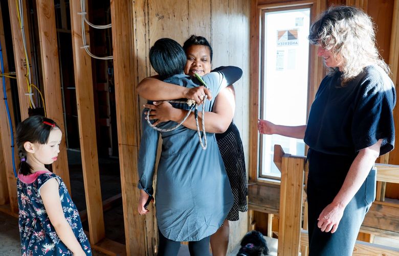 Milvia Berenice Pacheco Salvatierra, facing at center, hugs Yingzhao Liu as Liu’s daughter Sage, age seven, and Kelly Sommerfeld flank them on the second floor of the house that they will all own together along with Sommerfeld’s partner, Brandon Woodward, Tuesday, May 6, 2025 on Beacon Hill in Seattle. 230035